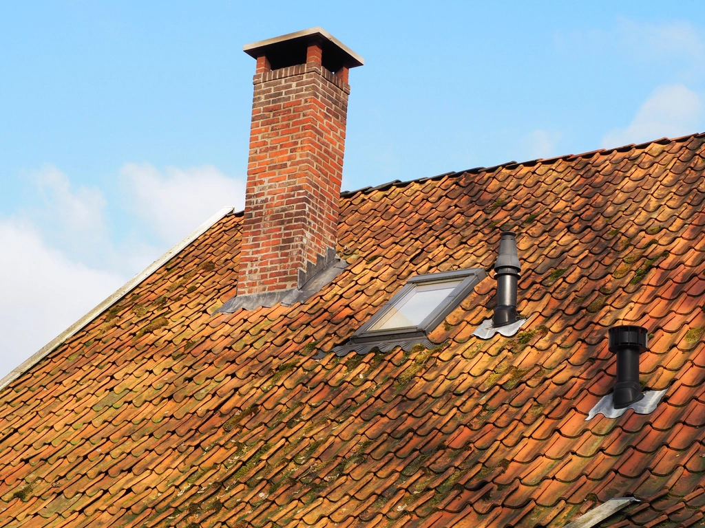 Brick chimney flue rising above a tiled roof